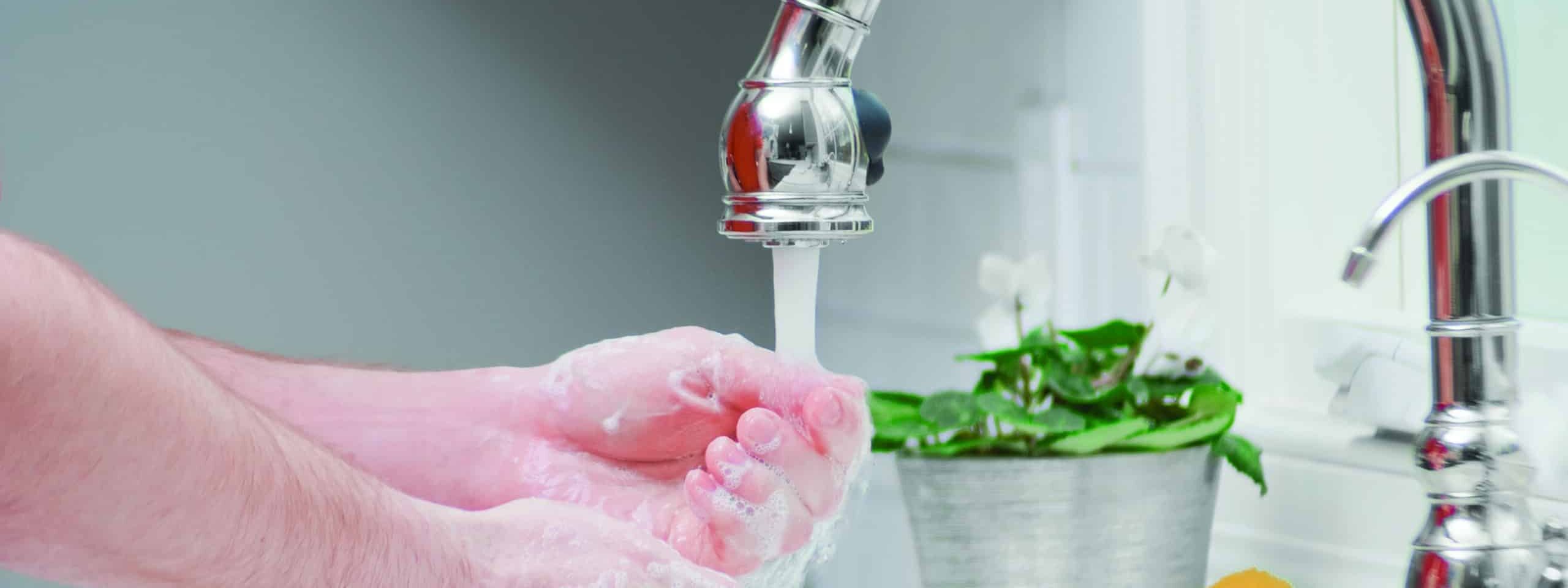 Person washing hands with soap under a running faucet in a kitchen setting